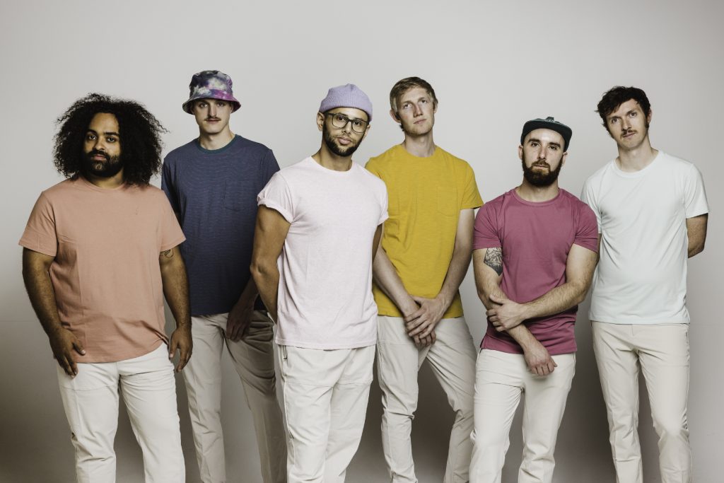 Joe Hertler & The Rainbow Seekers standing in front of a grey background.