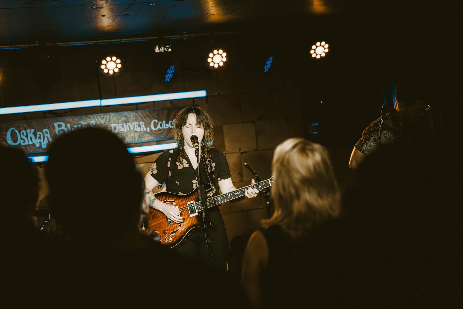 Amy Martin sings at the mic with a sunburst electric guitar at her album release show.