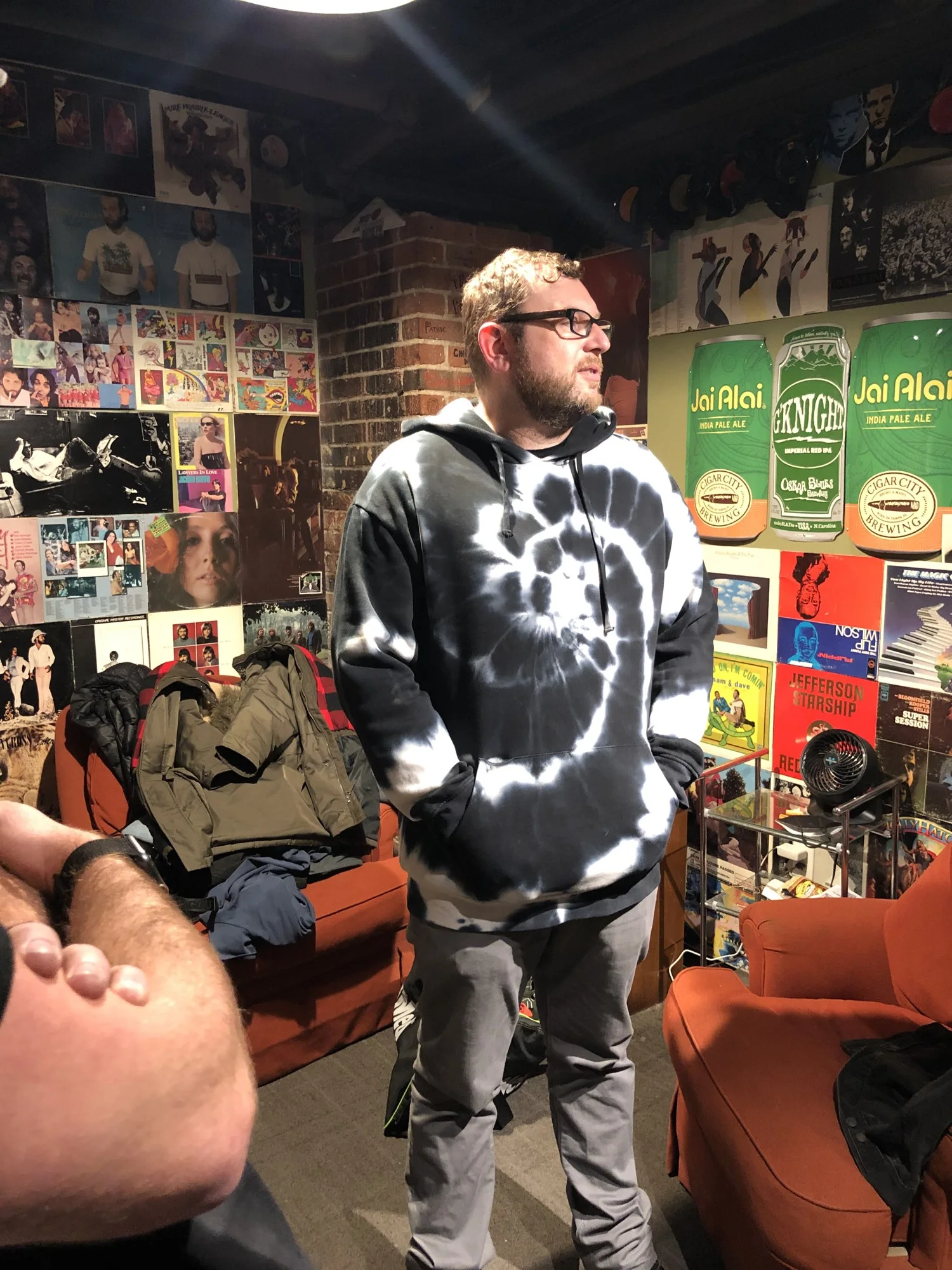 Tony Mason in a tie-dye hoodie in the Black Buzzard green room, walls covered in record sleeves.