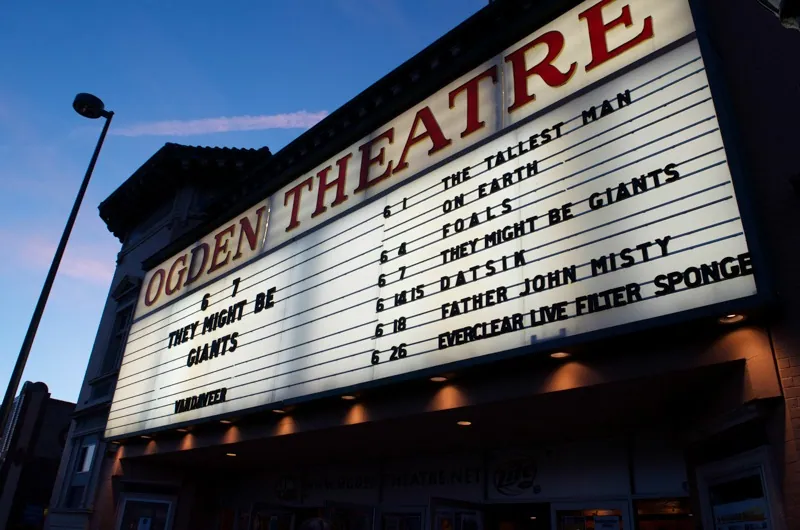 The Ogden Theatre marquee glows against a blue dusk sky, listing upcoming shows.