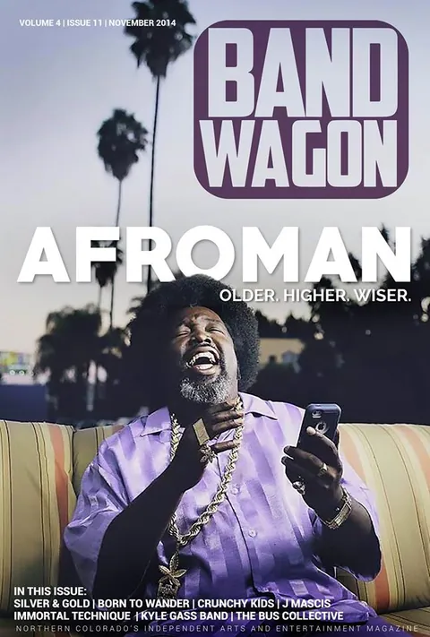Afroman laughs, head tilted back, on a striped couch in a purple shirt and gold chain, holding a phone.