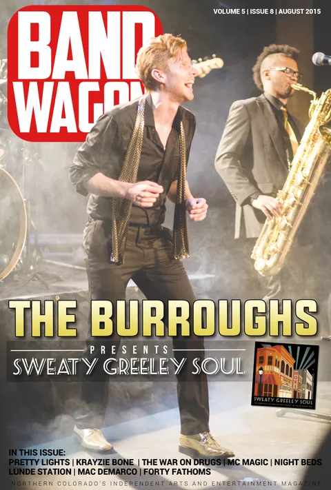 The Burroughs perform in smoky stage light, a singer in a black shirt dancing as a saxophonist plays.