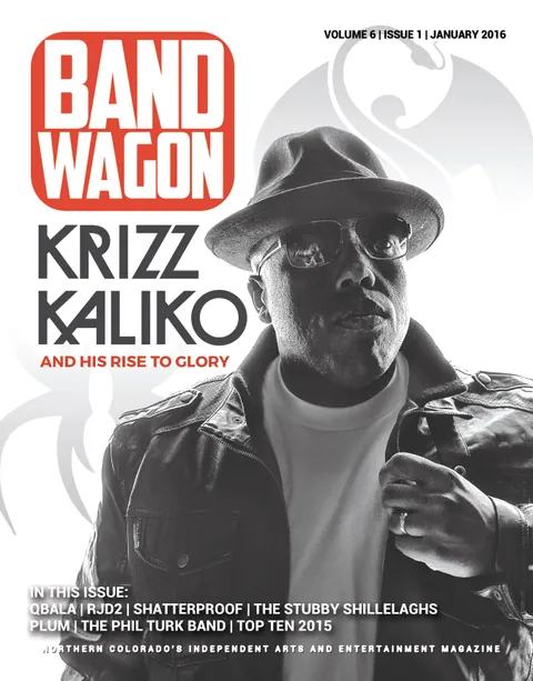 Krizz Kaliko poses in a fedora, glasses, white shirt, and dark jacket in a black-and-white portrait.