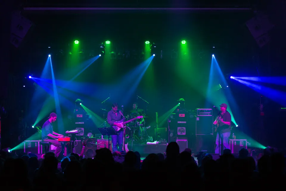 Dead Floyd performs under green and blue stage lights, with keyboards, guitar, and drums before a crowd.