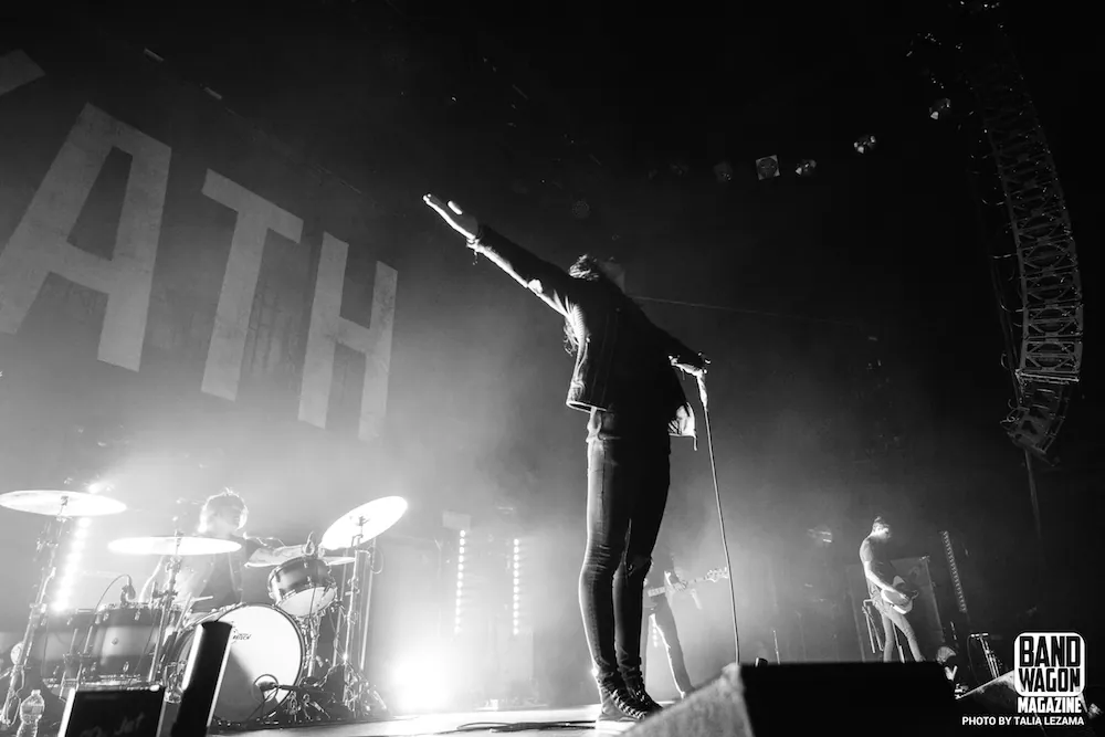 Underoath performs in black and white, with a singer arm raised at the mic, a drummer, and a guitarist.