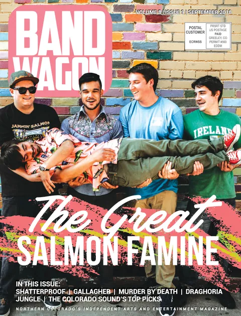 The Great Salmon Famine: five young men pose against a colorful brick wall, one carried horizontally by the others.