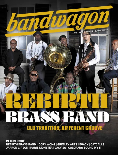 Rebirth Brass Band posing on a porch with a sousaphone, trumpet, saxophone, and trombone.