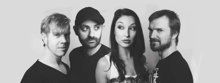 Black-and-white group portrait of four people in dark tops against a plain backdrop, with no instruments visible.