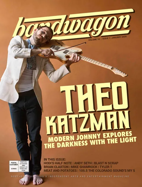 Theo Katzman, in a white blazer and barefoot, bows a tan electric guitar against an orange backdrop.