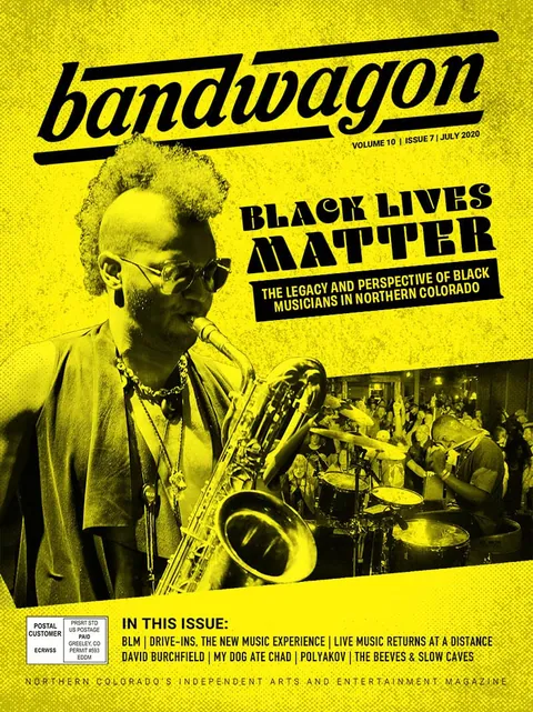 Saxophonist with curly hair and glasses performs as a drummer and crowd fill the club behind him.