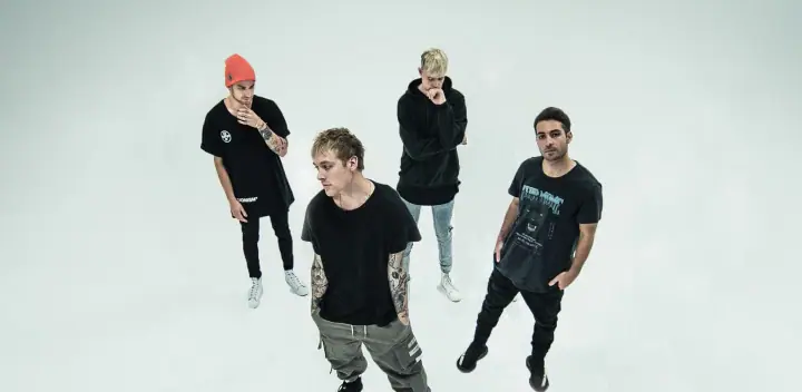 Four men in black shirts and hoodies pose in a bright white studio, shot from above, with no instruments visible.