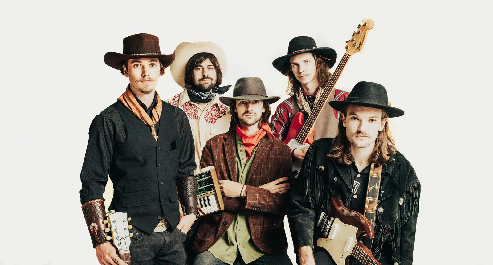 The Crooked Rugs pose in western hats and vests against a white backdrop, holding guitars and a bass.