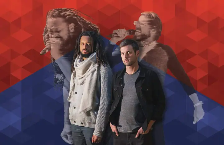 Two men pose before a red and blue geometric backdrop, with faded performers singing into mics behind them.