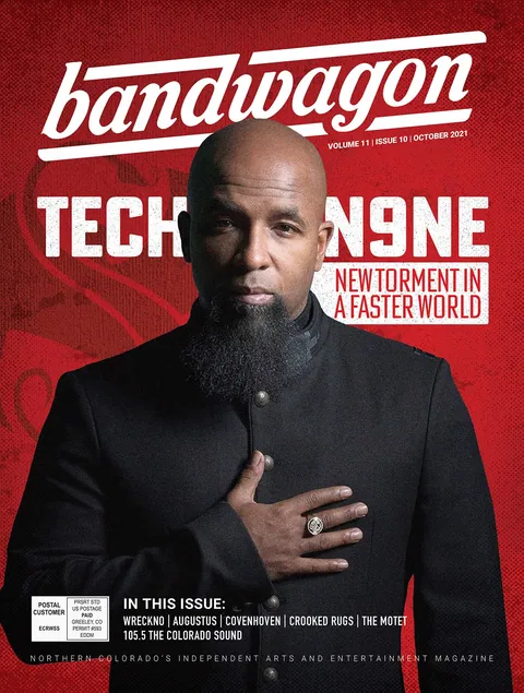 Tech N9ne poses in a black high-collared jacket, hand on chest, against a red backdrop on a BandWagon magazine cover.