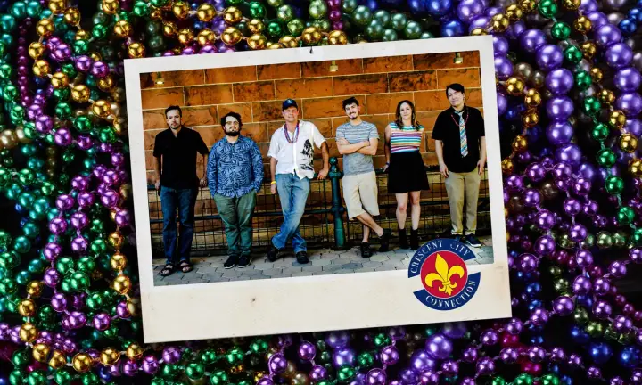 Six members of Crescent City Connection pose in a row against a brick wall, framed over Mardi Gras beads.