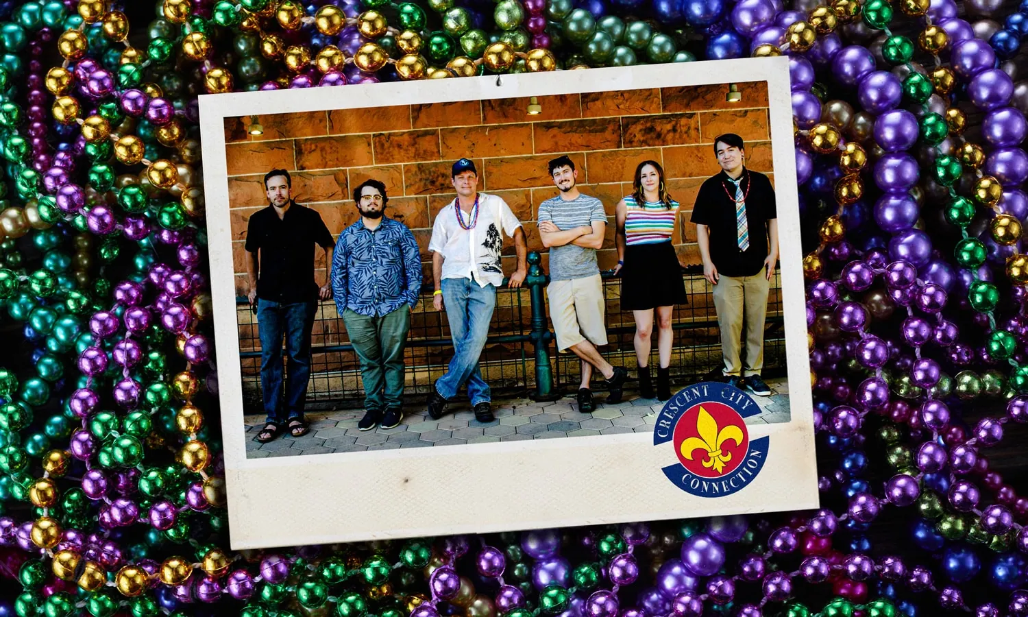 Six members of Crescent City Connection pose in a row against a brick wall, framed over Mardi Gras beads.
