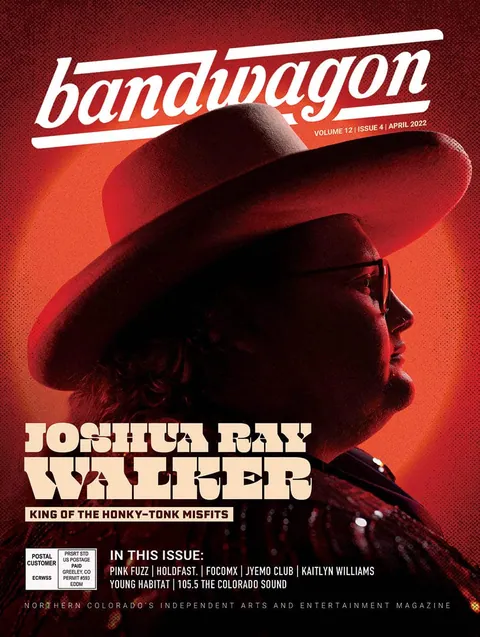 Joshua Ray Walker in a wide-brimmed hat and glasses, shown in profile against a red-lit backdrop.