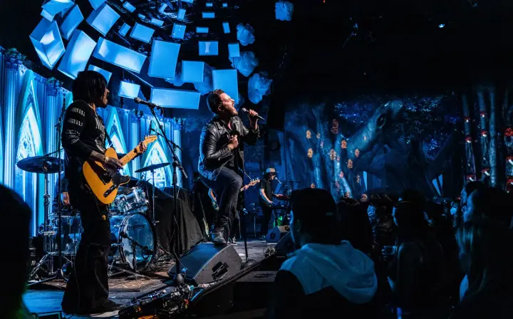 Elektric Animals perform on a blue-lit stage, with a singer in leather jacket, a guitarist, and a silhouetted crowd.