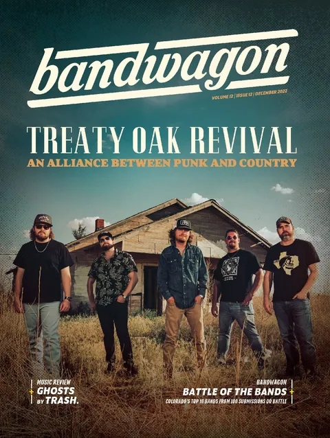 Treaty Oak Revival, five men in casual clothes and caps standing in tall dry grass before a weathered wooden house.