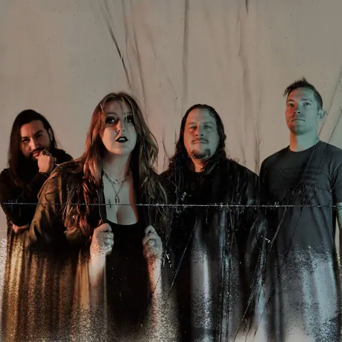 Heartsick Heroine band portrait: four members in dark clothing pose before a draped gray backdrop.