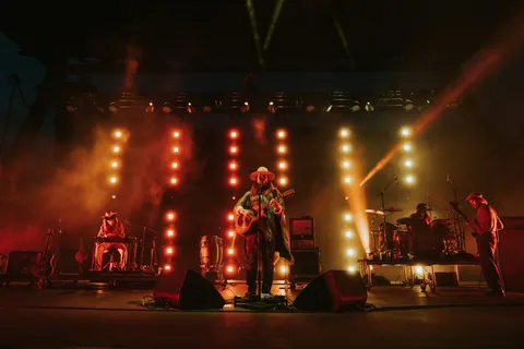 Kaleo performs at Red Rocks with a hatted guitarist, drummer, and keyboardist under red stage lights.