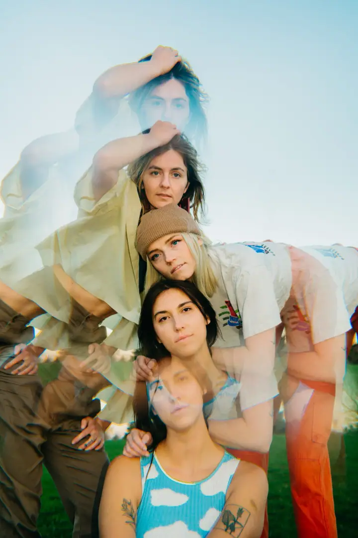 Overlapping multiple-exposure portrait of four women posing outdoors on green grass under a pale blue sky.