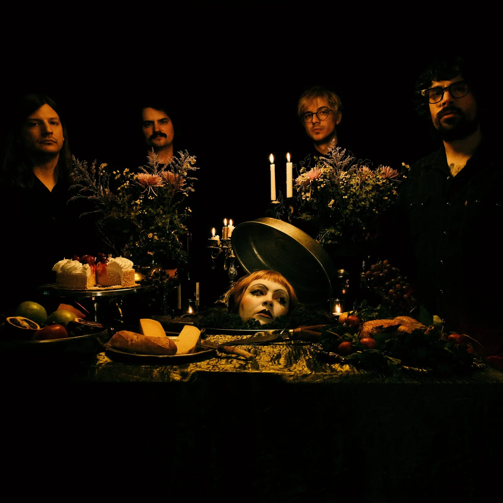 Bitchflower poses behind a candlelit gothic feast table with a doll's head on a platter.