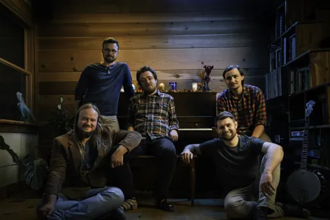 Tophouse band members pose in a wood-paneled room with a piano, a banjo, and shelves of records.