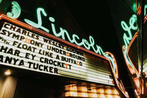 Illuminated marquee and green neon "Lincoln" script glowing above the theater entrance at night.