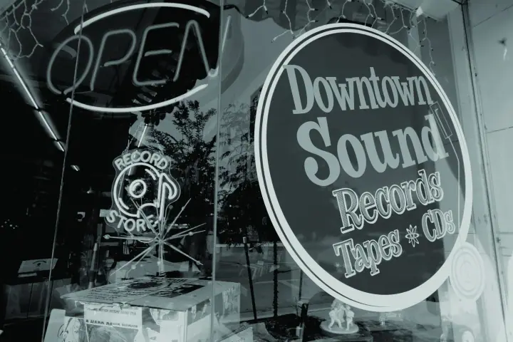 Window of the Downtown Sound record store with a lit OPEN neon sign and records displayed inside.